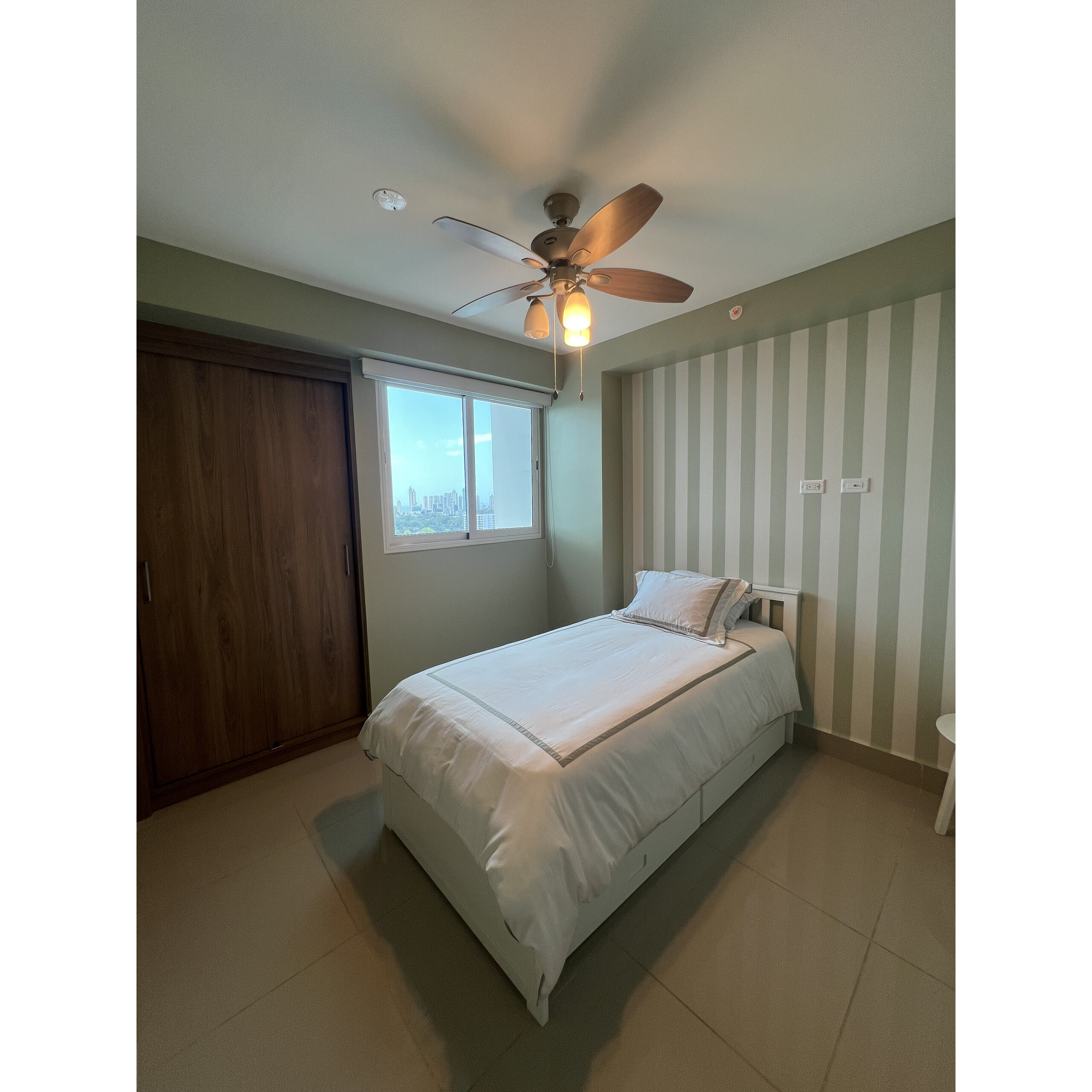 Recámara con cama individual, clóset de madera, ventana y ventilador de techo.