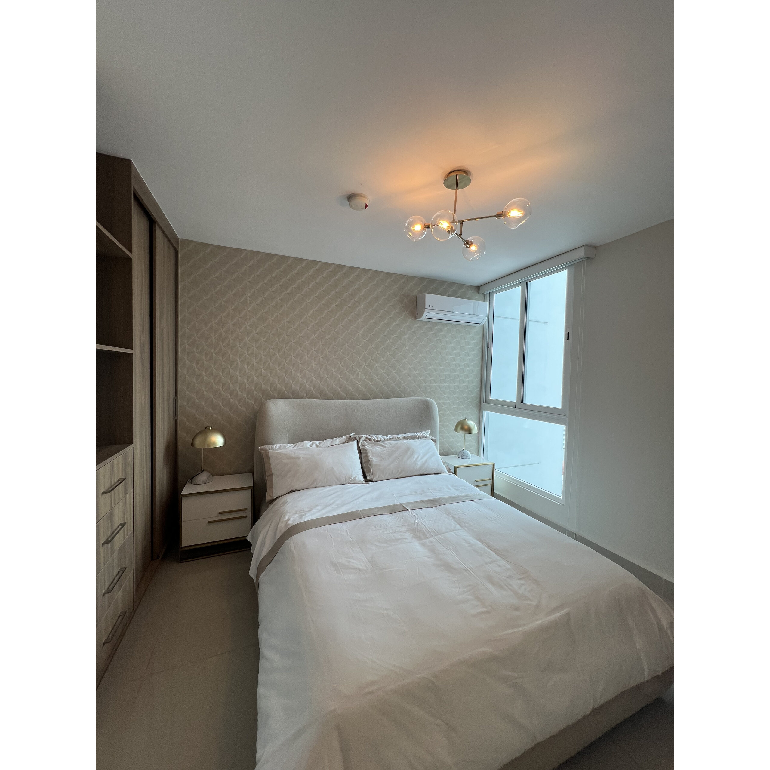 Recámara moderna con cama doble, burós, clóset y ventana grande.
