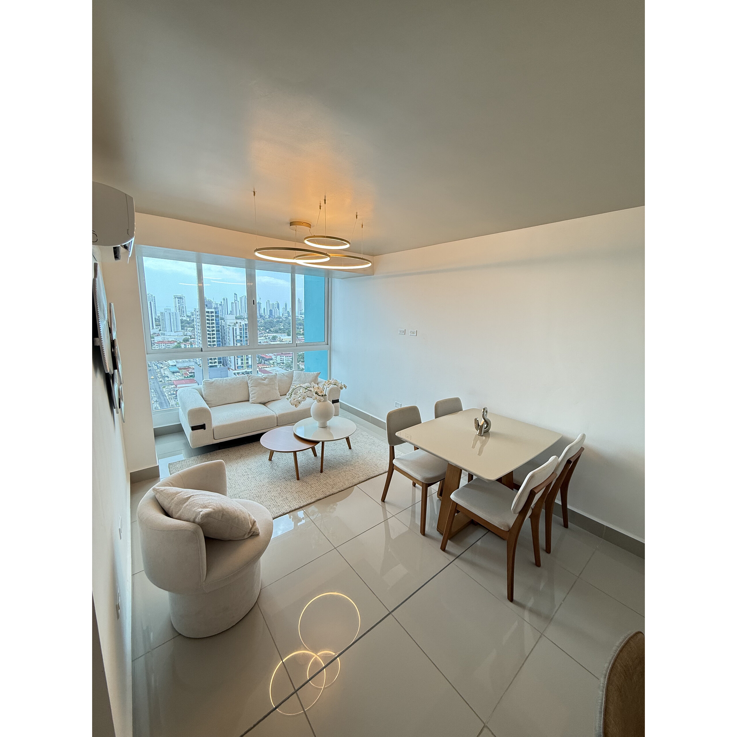 Sala-comedor moderna con sofá claro, mesa de comedor y vista urbana.