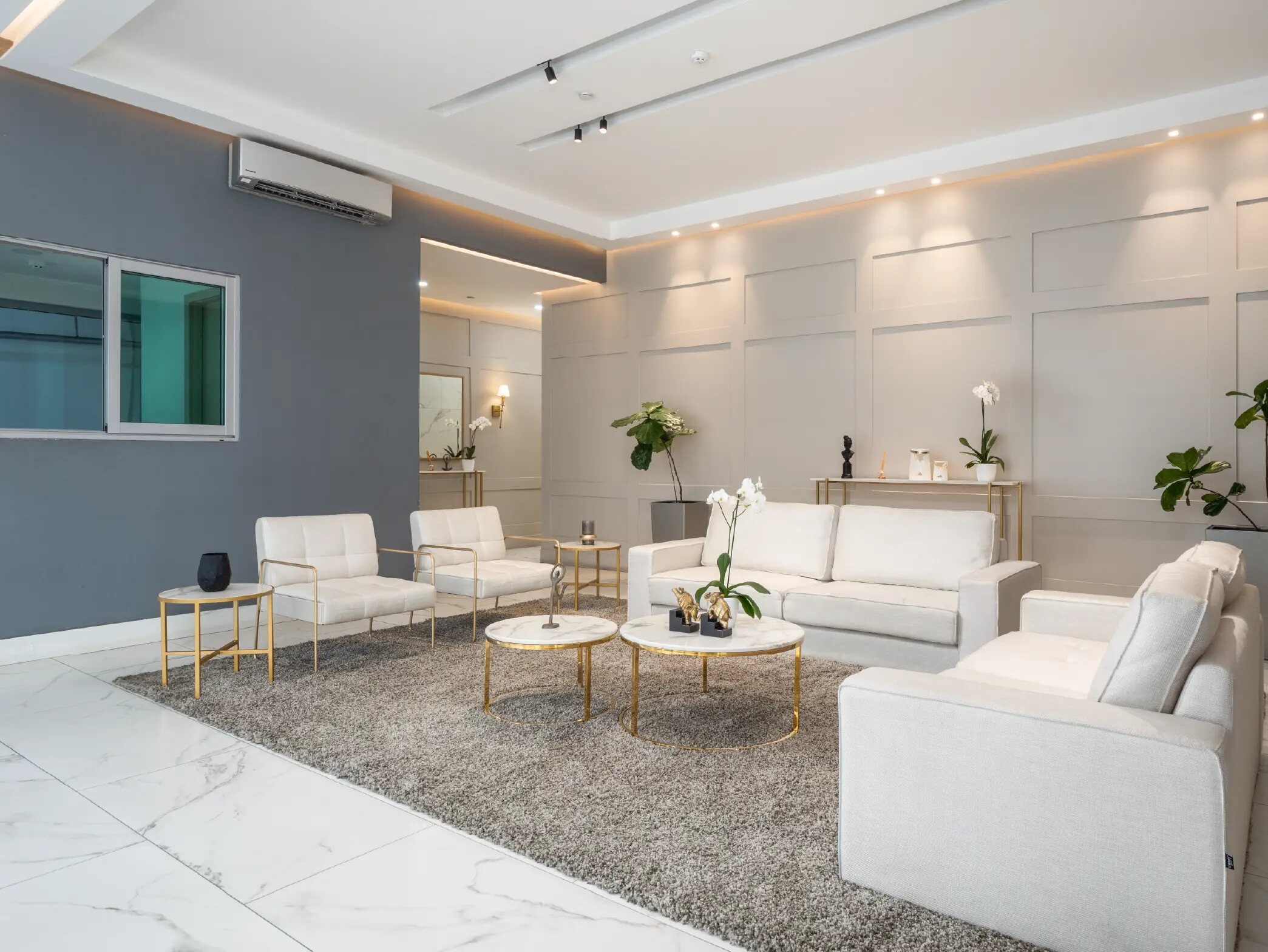 Lobby moderno con sofás blancos, mesas doradas y plantas decorativas.