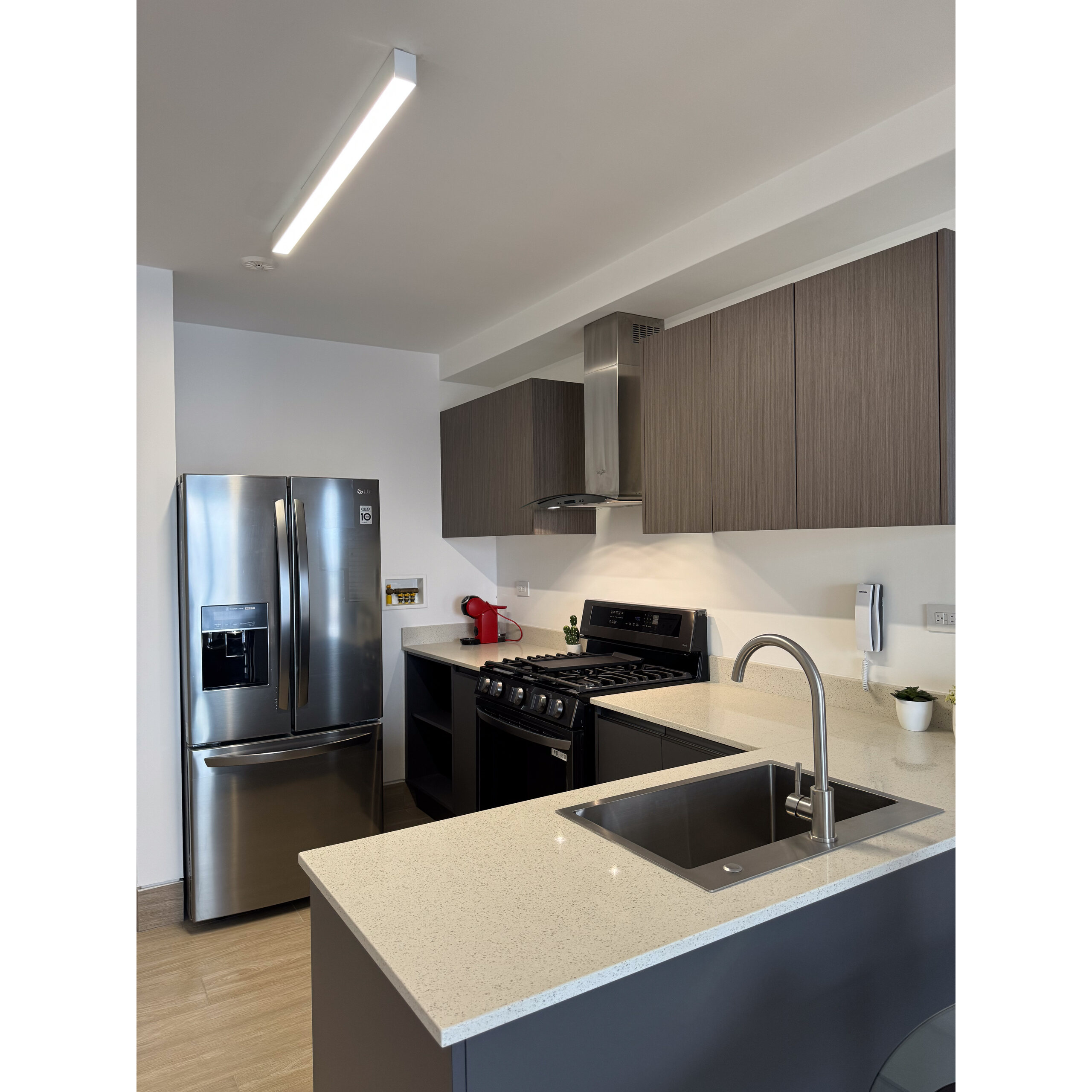 Cocina moderna con isla, fregadero, refrigerador de acero y gabinetes oscuros.