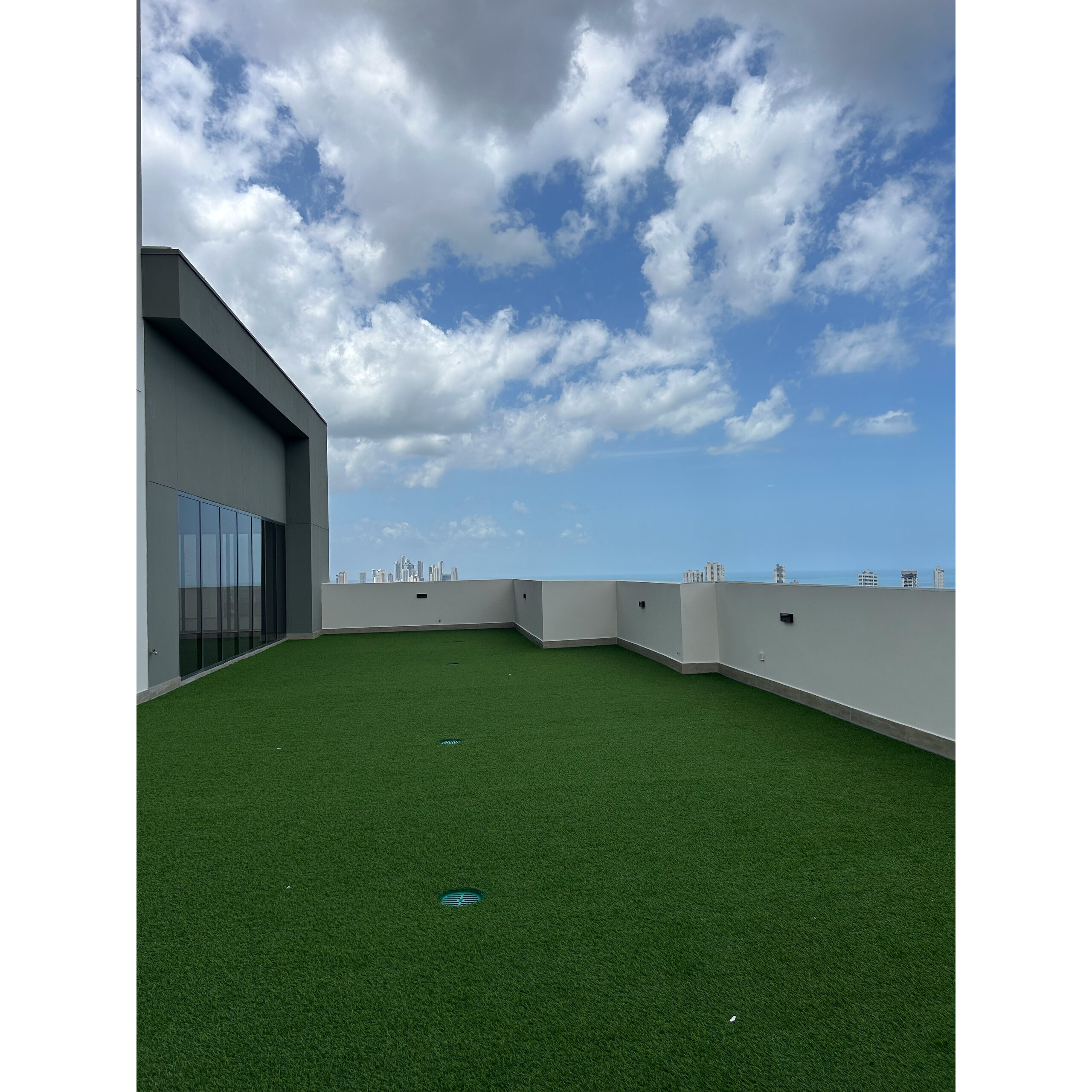Rooftop con piso verde, barandal blanco y cielo nublado.