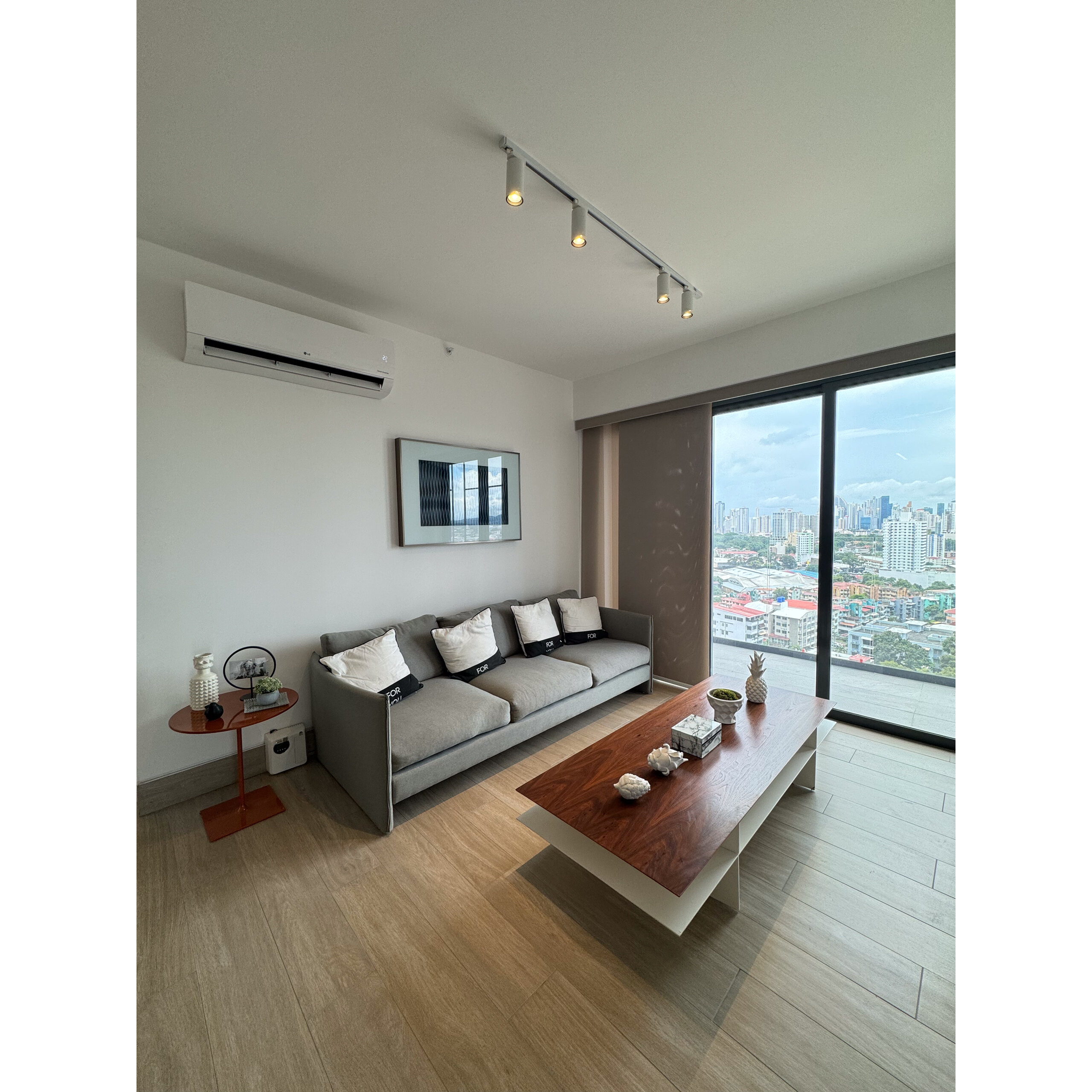 Sala moderna con sofá gris, mesa de centro de madera y ventanal amplio.