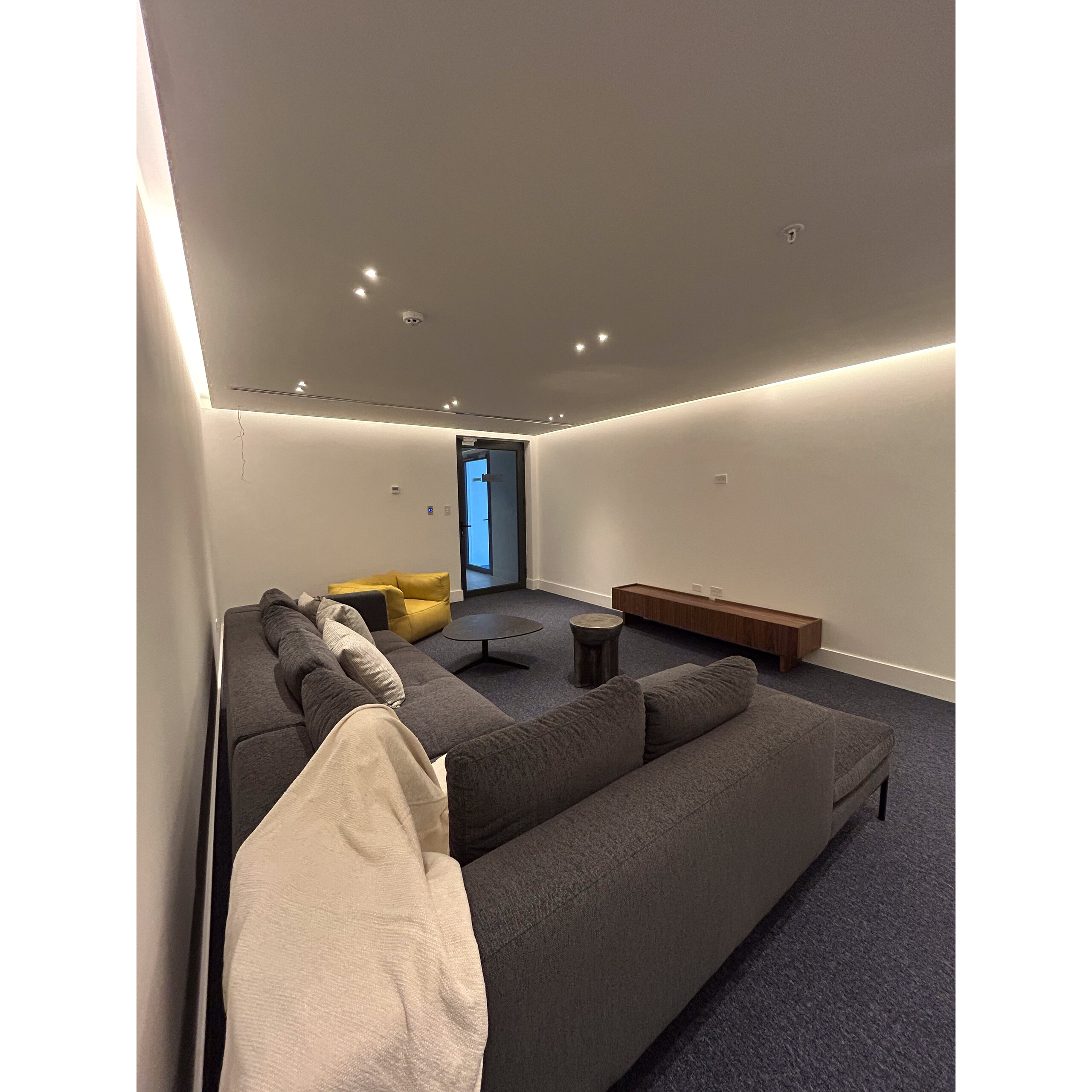 Sala de entretenimiento con sofá gris, sillón amarillo y mesas bajas.