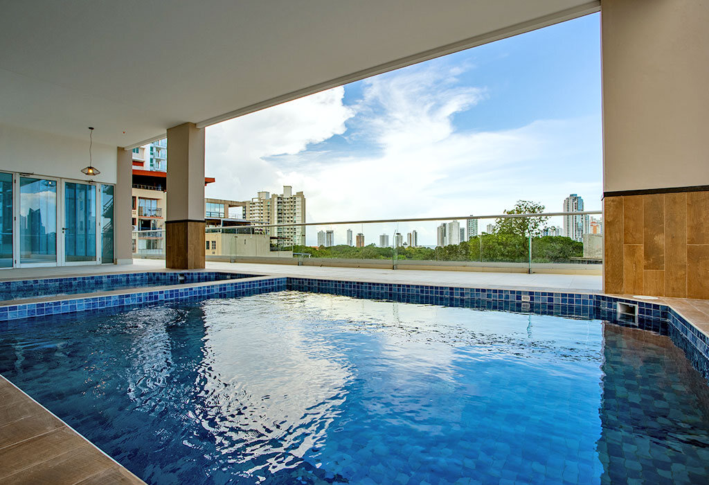Piscina techada con barandal de vidrio y vista urbana.