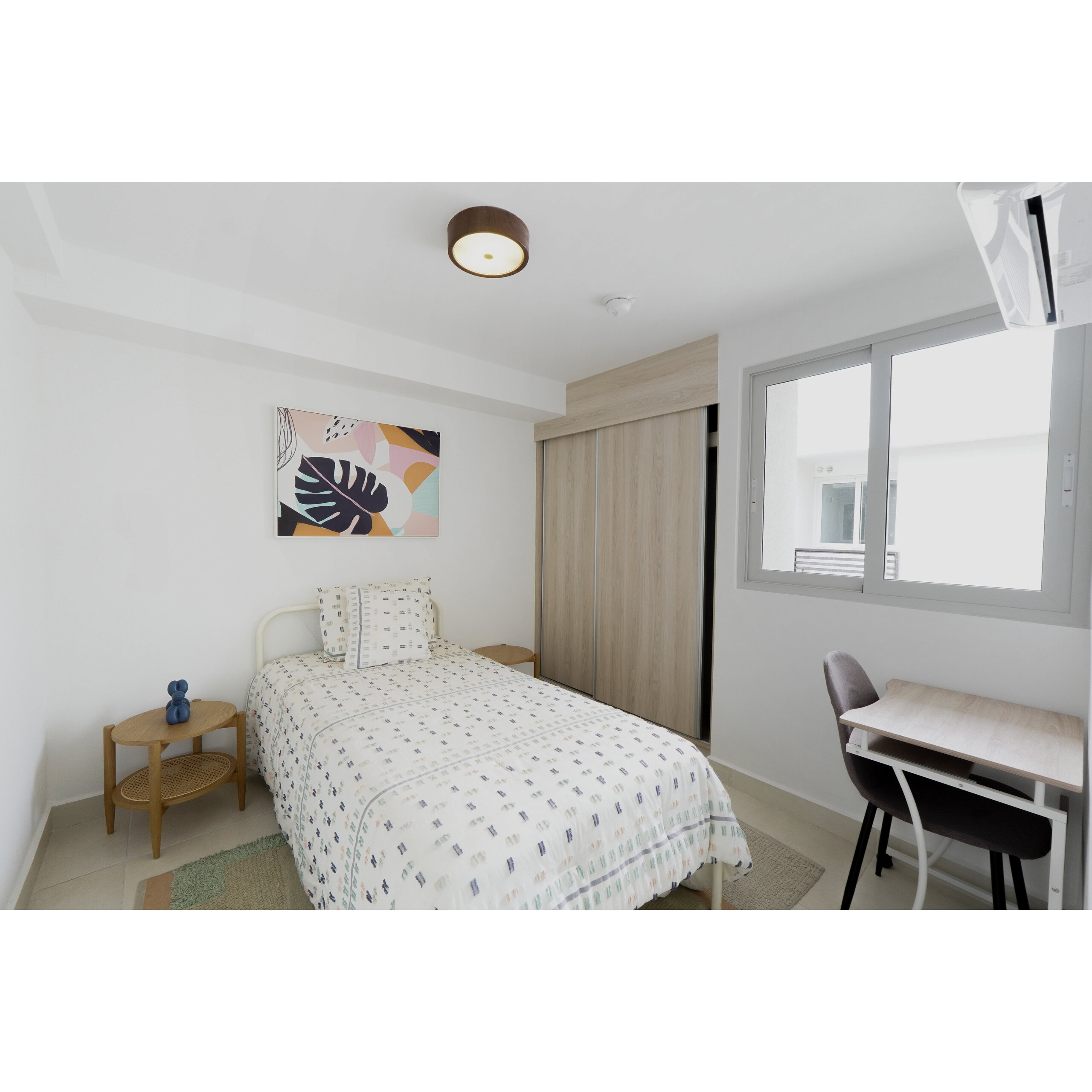 Recámara luminosa con cama individual, clóset, escritorio y ventana.