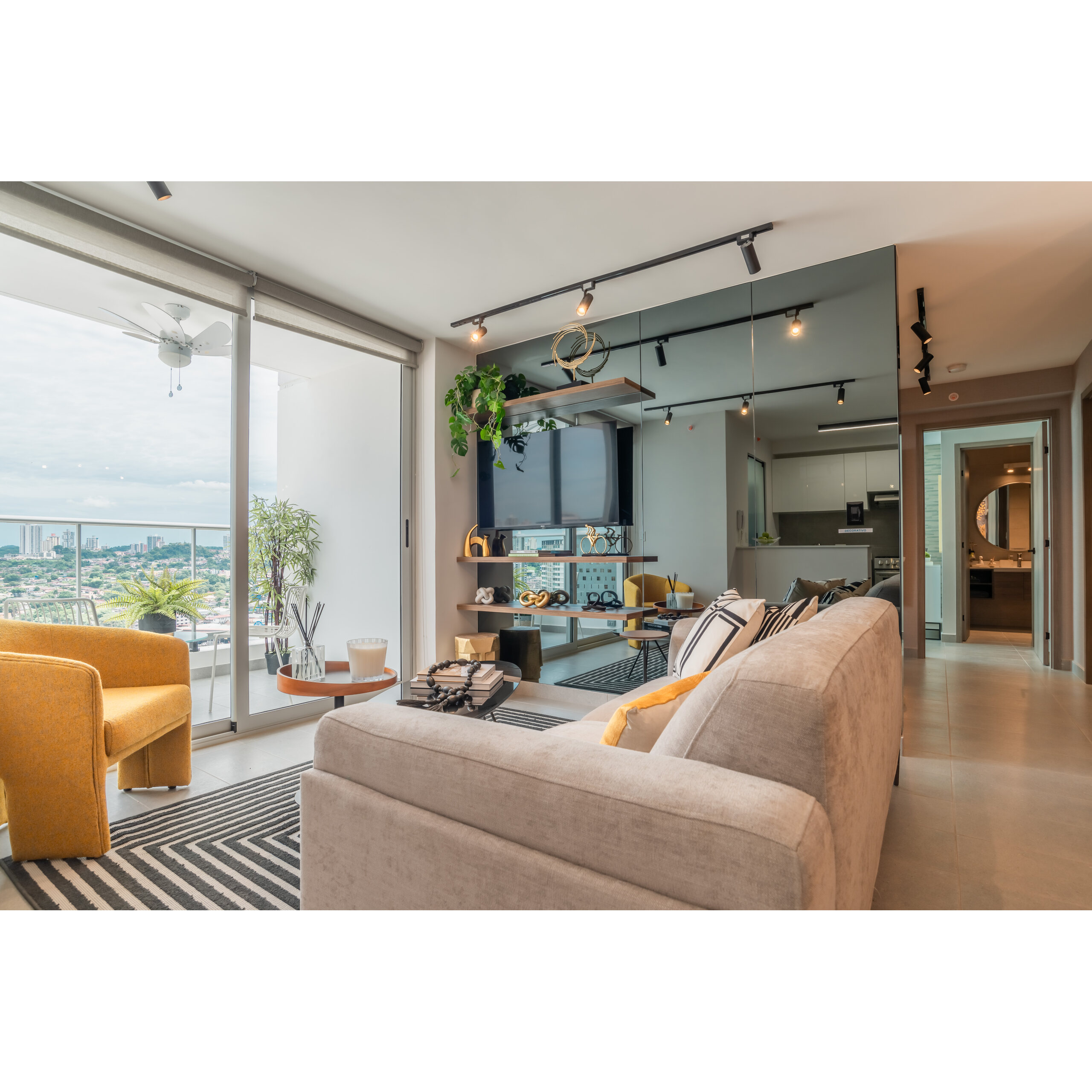 Sala moderna con sofá beige, sillón amarillo, balcón y vista exterior.