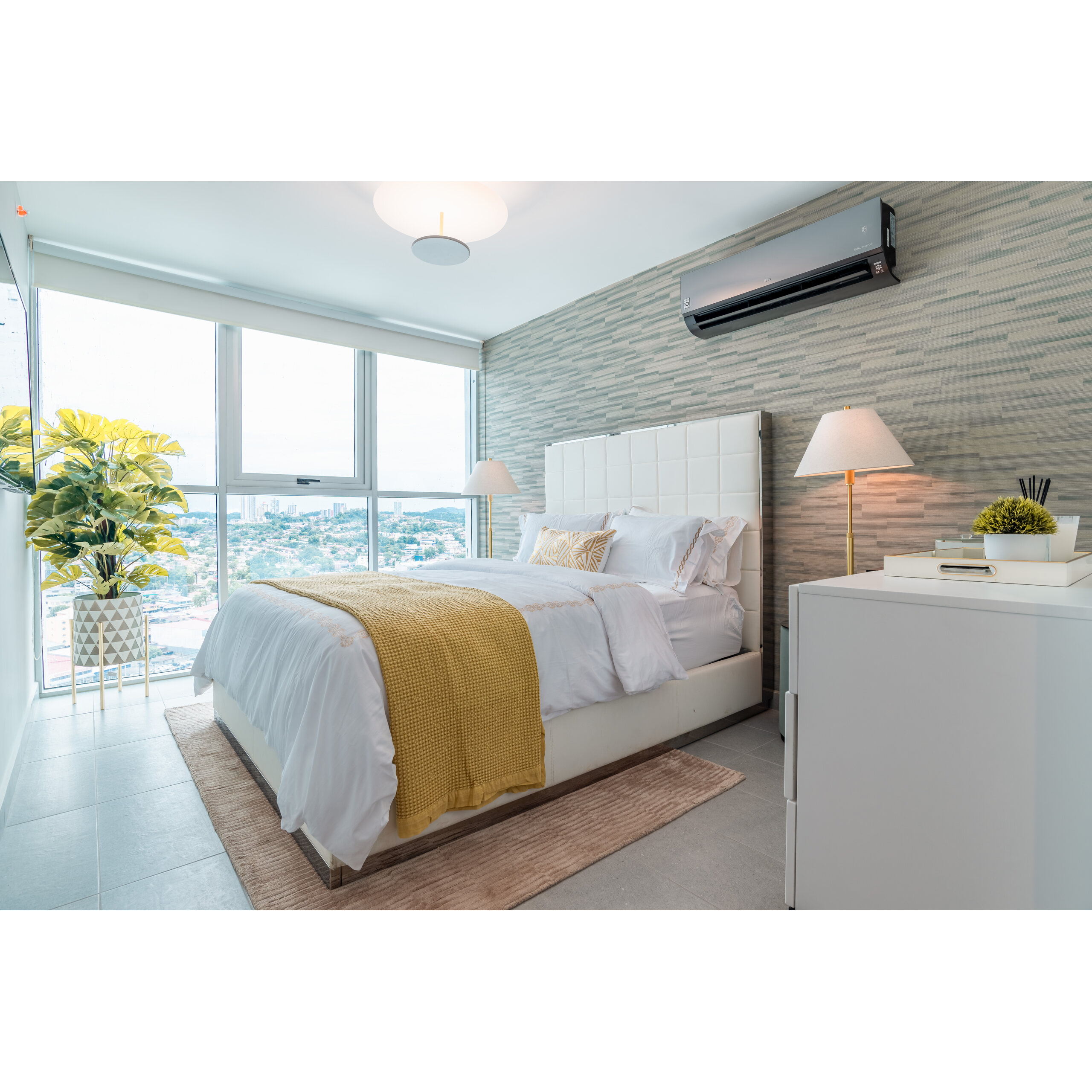 Recámara moderna con cama blanca, ventana amplia y vista urbana.