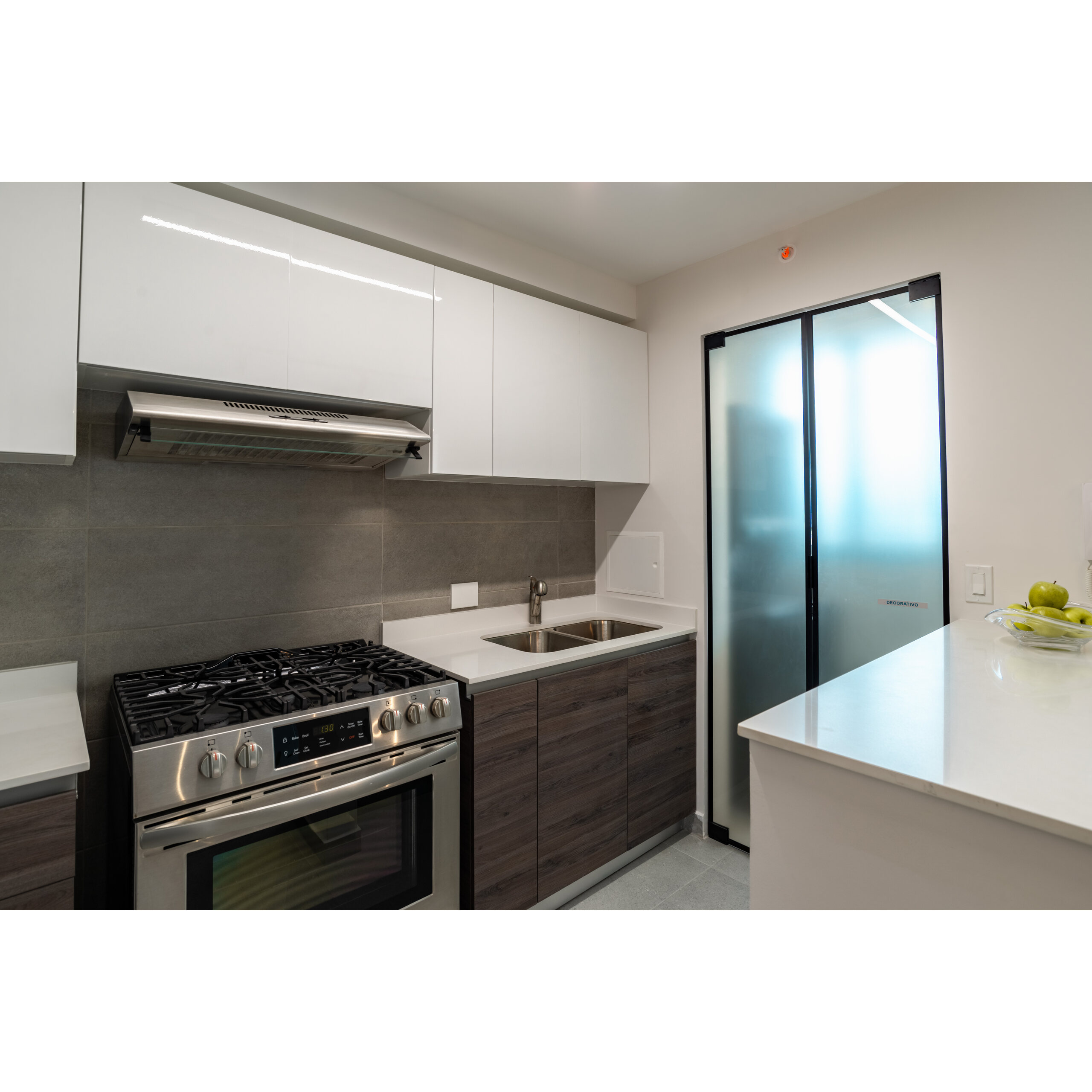 Cocina moderna con estufa, fregadero, gabinetes blancos y puerta de vidrio esmerilado.