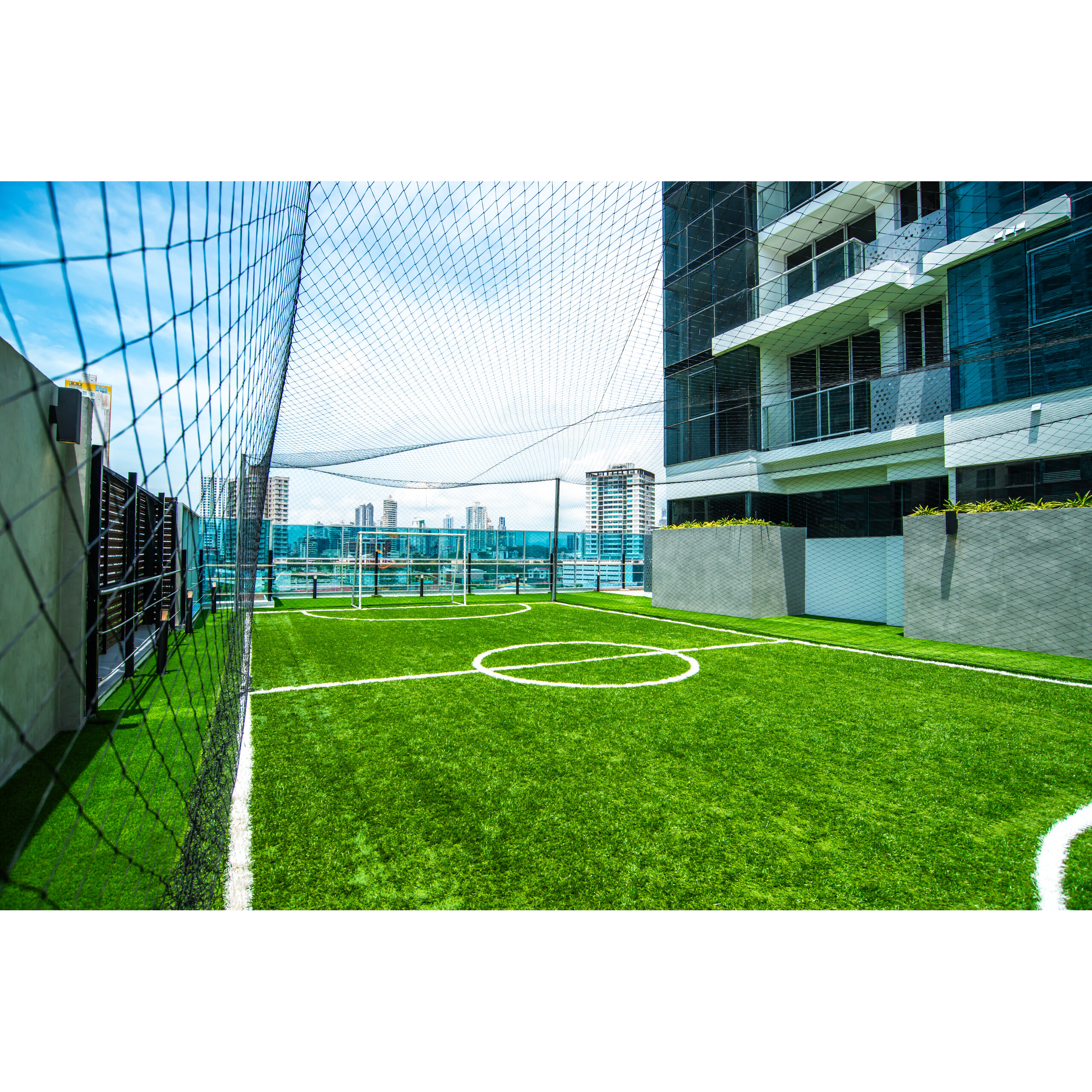 Cancha de pasto sintético en la azotea de Rise - Park Square, junto a un edificio moderno.