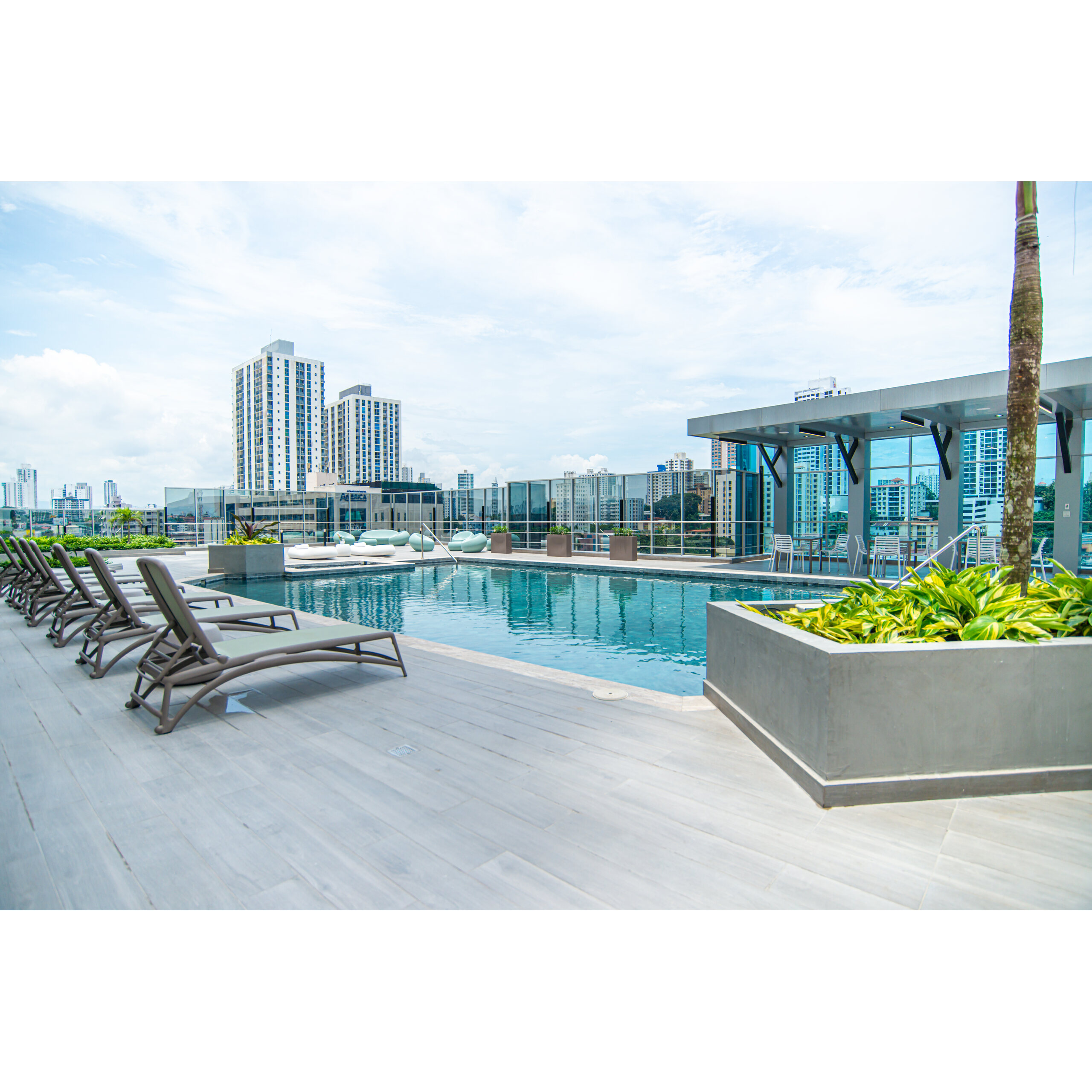 Piscina exterior en Rise - Park Square con camastros y vista urbana.